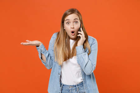 Shocked young woman girl in casual denim clothes posing isolated on orange background studio portrait.の写真素材