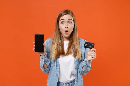 Shocked young woman girl in casual denim clothes posing isolated on orange wall background.の写真素材