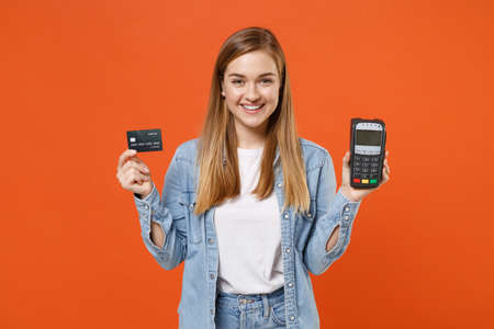 Smiling young woman in denim clothes isolated on orange background.