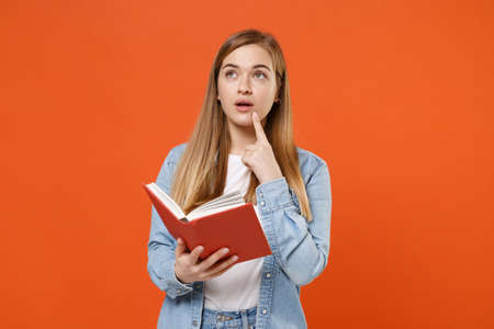 Pensive young woman girl in casual denim clothes posing isolated on orange background studio portrait.の写真素材