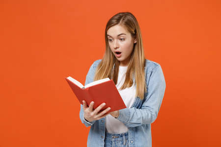 Shocked amazed young woman girl in casual denim clothes posing isolated on bright orange wall background studio portrait.の写真素材