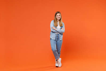 Smiling young woman girl in casual denim clothes posing isolated on bright orange wall background studio portrait.の写真素材