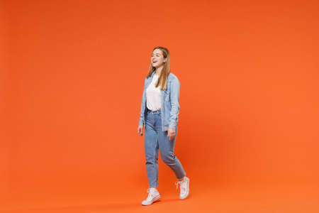 Side view of laughing young woman girl in casual denim clothes posing isolated on orange wall...