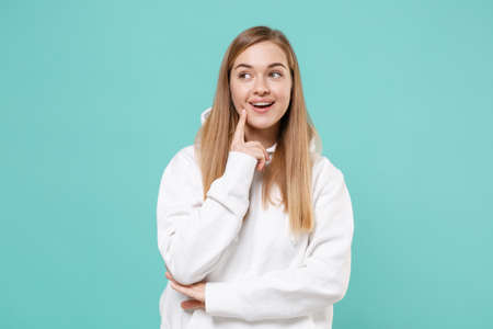 Pensive young woman girl in casual white hoodie posing isolated on blue turquoise background studio portrait.の写真素材