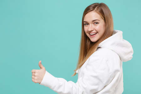 Side view of smiling young woman in casual white hoodie posing isolated on blue turquoise background...