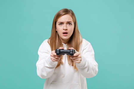 Shocked young woman girl in casual white hoodie posing isolated on blue turquoise background studio portrait. People sincere emotions lifestyle concept. Mock up copy space. Play game with joystick.の写真素材