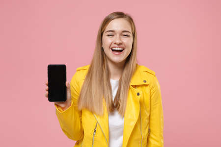 Laughing young woman girl in yellow leather jacket posing isolated on pastel pink background studio...