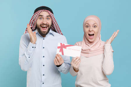Surprised young couple friends arabian muslim man wonam in keffiyeh kafiya ring igal agal hijab clothes isolated on blue background.の写真素材