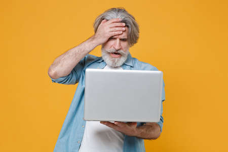 Preoccupied elderly gray-haired mustache bearded man in casual blue shirt isolated on yellow background.の写真素材