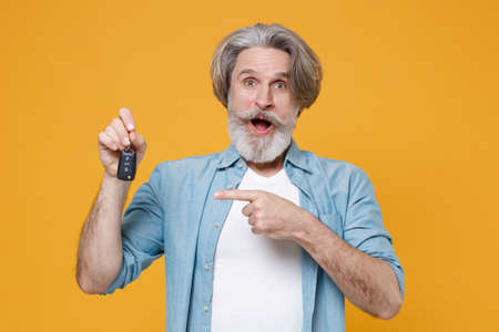 Shocked elderly gray-haired mustache bearded man in casual blue shirt posing isolated on yellow wall background studio.の写真素材
