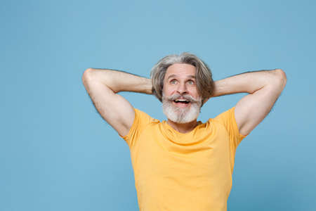 Excited elderly gray-haired mustache bearded man in casual yellow t-shirt isolated on blue...