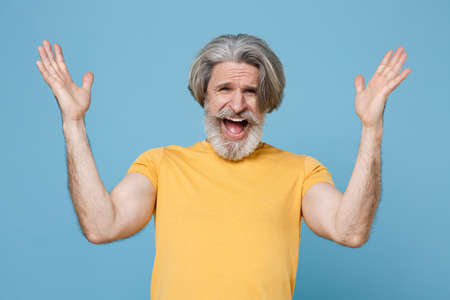 Angry irritated elderly gray-haired mustache bearded man in casual yellow t-shirt posing isolated on...