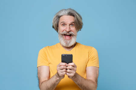 Surprised elderly gray-haired mustache bearded man in casual yellow t-shirt posing isolated on blue background.の写真素材