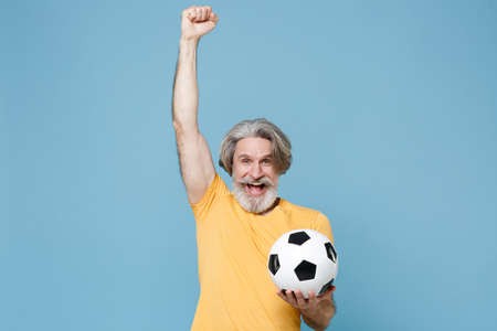Happy elderly gray-haired mustache bearded man in yellow t-shirt isolated on blue wall background.の写真素材