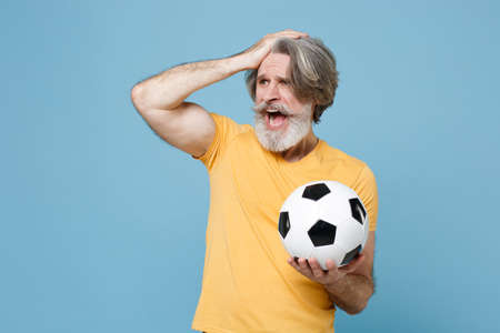 Shocked displeased elderly gray-haired mustache bearded man in yellow t-shirt isolated on blue background.の写真素材