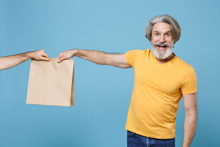 Cheerful elderly gray-haired mustache bearded man in casual yellow t-shirt isolated on blue...