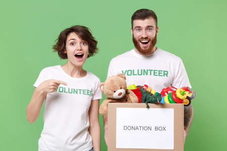 Excited two friends couple in volunteer t-shirt isolated on green background. Voluntary free work...