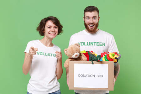 Smiling friends couple in volunteer t-shirt isolated on green background. Voluntary free work...