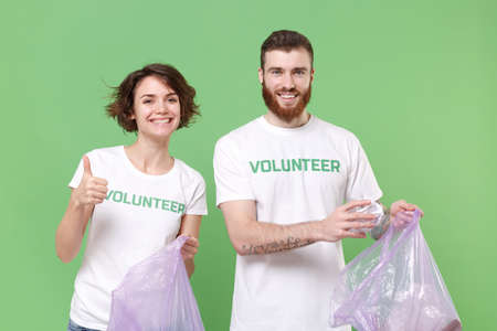 Smiling friends couple in volunteer t-shirt isolated on green background. Voluntary free work...