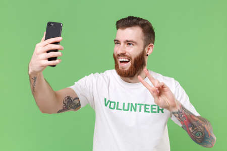 Laughing man in white volunteer t-shirt isolated on pastel green background. Voluntary free work...