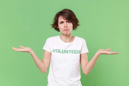 Dissatisfied young brunette woman in white volunteer t-shirt isolated on pastel green background...