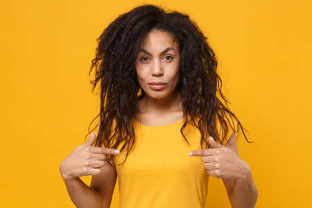 Perplexed confused young african american woman girl in casual t-shirt posing isolated on yellow orange background. People lifestyle concept. Mock up copy space. Pointing index fingers on herself.の写真素材