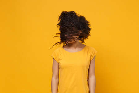 Young african american woman girl in casual t-shirt posing isolated on yellow orange wall background studio portrait. People lifestyle concept. Mock up copy space. Fooling around with fluttering hair.の写真素材