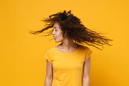 Beautiful young african american woman girl in casual t-shirt posing isolated on yellow orange...