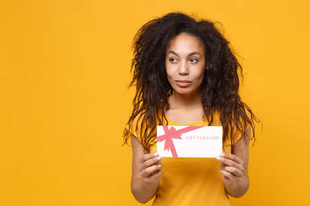 Smiling pensive young african american woman girl in casual t-shirt posing isolated on yellow orange...