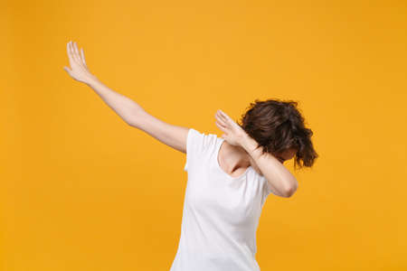 Young brunette woman in white t-shirt posing isolated on yellow orange wall background studio portrait. People sincere emotions lifestyle concept. Mock up copy space. Showing DAB dance gesture.の写真素材
