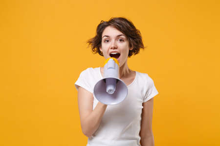 Excited young brunette woman girl in white t-shirt posing isolated on yellow orange wall background studio portrait. People sincere emotions lifestyle concept. Mock up copy space. Scream in megaphone.の写真素材