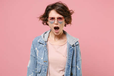 Shocked irritated young brunette woman girl in casual denim jacket eyeglasses posing isolated on pastel pink wall background studio portrait. People lifestyle concept. Mock up copy space. Swearing.の写真素材