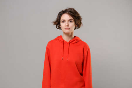Attractive beautiful young brunette woman girl in casual red hoodie posing isolated on grey background studio portrait. People sincere emotions lifestyle concept. Mock up copy space. Looking camera.の写真素材
