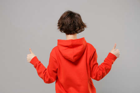 Back rear view of young brunette woman girl in casual red hoodie posing isolated on grey background studio portrait. People sincere emotions lifestyle concept. Mock up copy space. Showing thumbs up.の写真素材