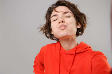 Close up of funny young brunette woman in casual red hoodie posing isolated on grey background....