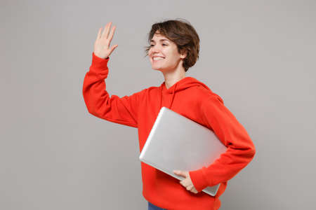 Joyful young brunette woman in casual red hoodie posing isolated on grey background. People...