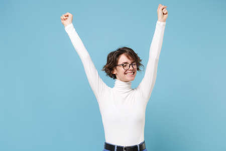 Happy young brunette woman girl in casual white clothes, eyeglasses posing isolated on pastel blue background. People lifestyle concept. Mock up copy space. Doing winner gesture keeping eyes closed.の写真素材