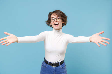 Joyful young brunette woman girl in casual white clothes eyeglasses posing isolated on pastel blue background. People lifestyle concept. Mock up copy space. Standing with outstretched hands for hugs.の写真素材