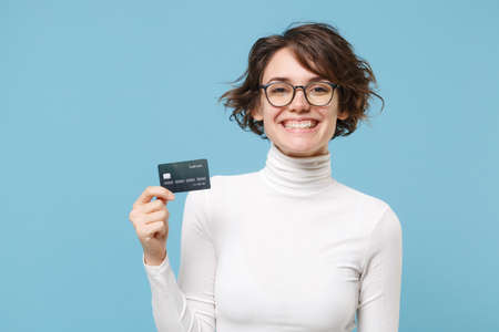 Cheerful young brunette woman girl in casual white clothes eyeglasses posing isolated on pastel blue background studio portrait. People lifestyle concept. Mock up copy space. Hold credit bank card.の写真素材
