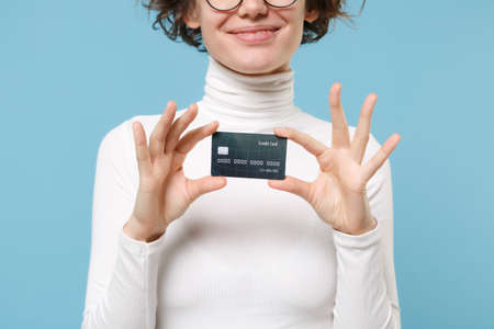 Cropped image of young brunette woman girl in casual white clothes eyeglasses posing isolated on pastel blue background in studio. People lifestyle concept. Mock up copy space. Hold credit bank card.の写真素材