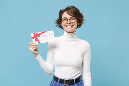 Cheerful young brunette woman girl in casual white clothes eyeglasses posing isolated on pastel blue background studio portrait. People lifestyle concept. Mock up copy space. Hold gift certificate.の写真素材