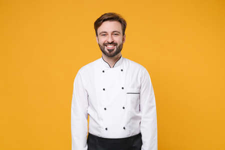 Smiling young bearded male chef cook or baker man in white uniform shirt posing isolated on yellow orange wall background studio portrait. Cooking food concept. Mock up copy space. Looking camera.の写真素材