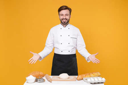 Cheerful young bearded male chef cook or baker man in white uniform shirt posing isolated on yellow...