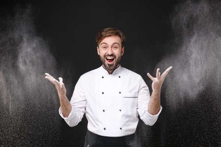 Surprised young bearded male chef cook or baker man in white uniform shirt posing isolated on black...