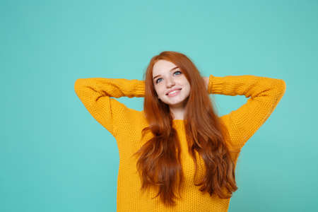 Pensive young redhead woman girl in yellow sweater posing isolated on blue turquoise wall background studio portrait. People lifestyle concept. Mock up copy space. Looking up with hands behind head.の写真素材