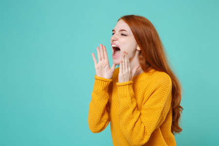 Crazy young redhead woman girl in yellow sweater posing isolated on blue turquoise background....