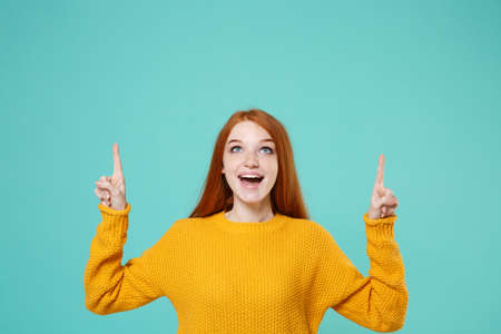 Amazed young redhead woman girl in yellow sweater posing isolated on blue turquoise wall background...