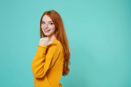 Side view of funny young redhead woman girl in yellow sweater posing isolated on blue turquoise...