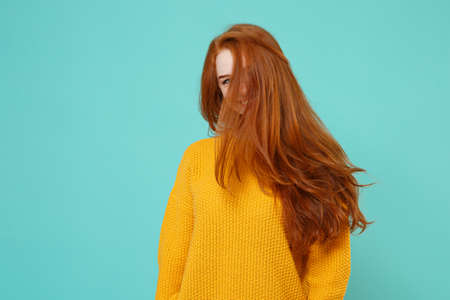 Beautiful young redhead woman girl in yellow sweater posing isolated on blue turquoise wall background studio portrait. People lifestyle concept. Mock up copy space. Having fun with fluttering hair.の写真素材