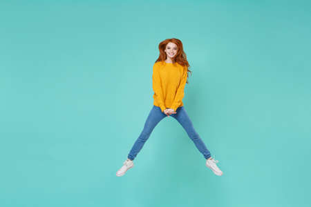 Smiling young redhead woman girl in yellow knitted sweater posing isolated on blue turquoise...